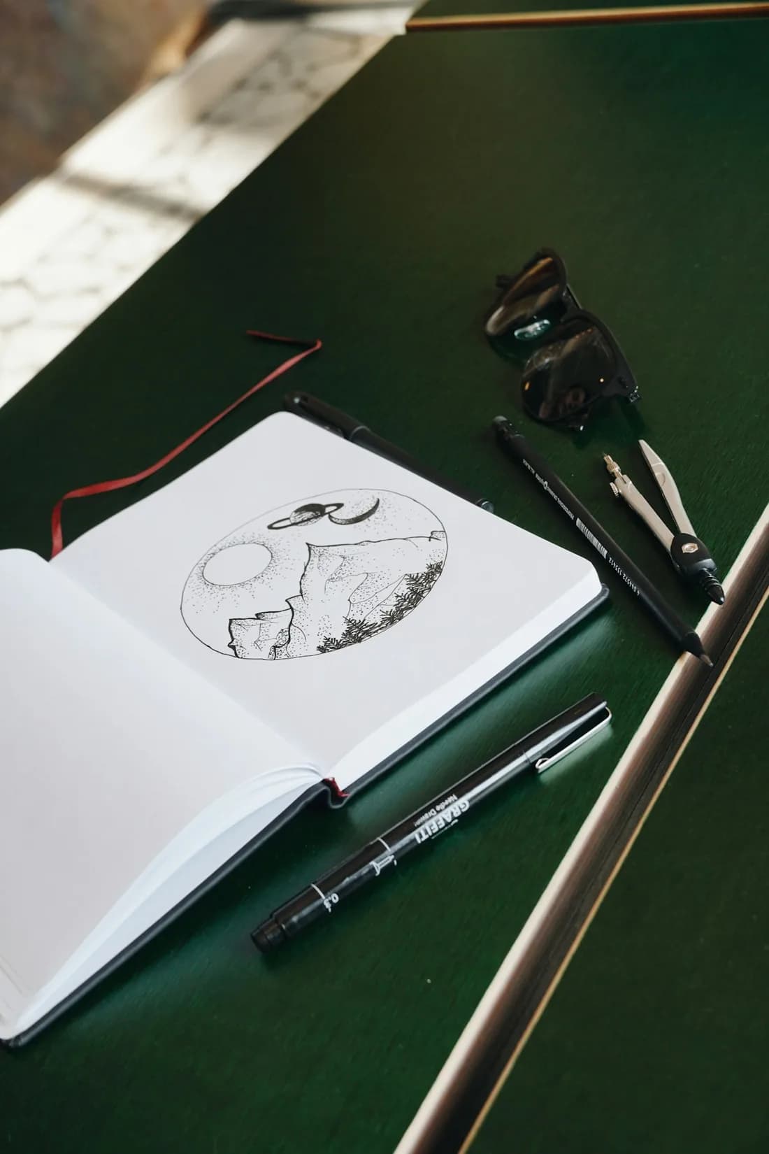 An open sketchbook with a pen drawing of mountains and planets